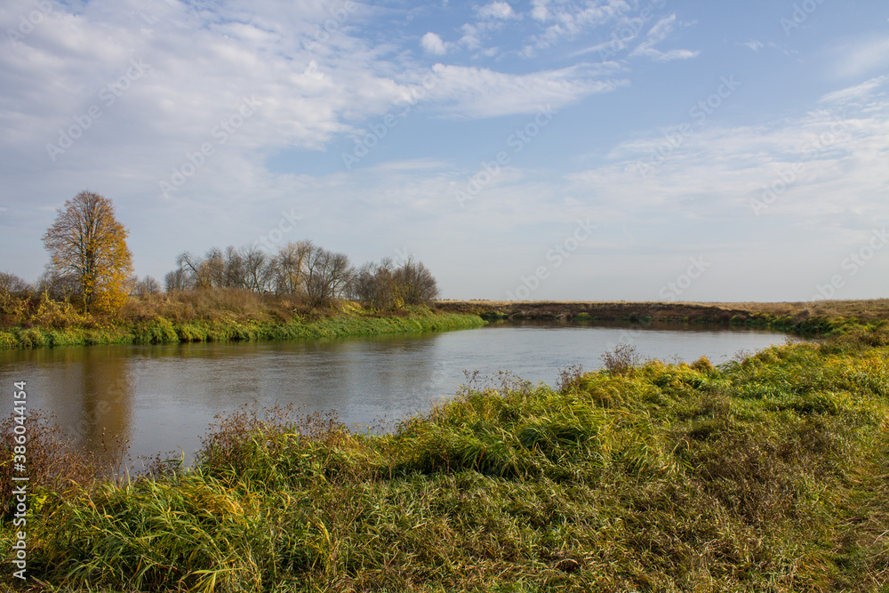 Autumn landscape - bend of the river with yellow grass and reflection of the cloudy sky and space for copying