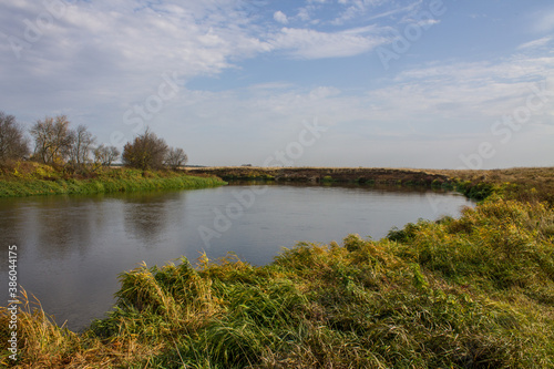 Fototapeta Naklejka Na Ścianę i Meble -  Autumn landscape - bend of the river with yellow grass and reflection of the cloudy sky and space for copying