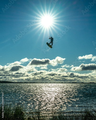 A man kiteboarding on Long Island jumps high into the sky and is silhouetted against the sun.