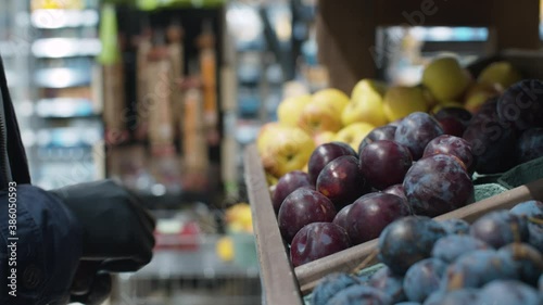 Close up male hand in protective latex gloves choosing plums in the supermarket. Protection against a viral epidemic