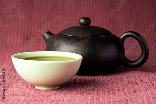 Chinese tea steaming in a small green teacup isolated with a black background and red surface