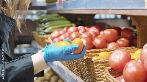 Close up female hand in protective latex gloves buying yellow tomatoes in the supermarket. Protection against a viral epidemic
