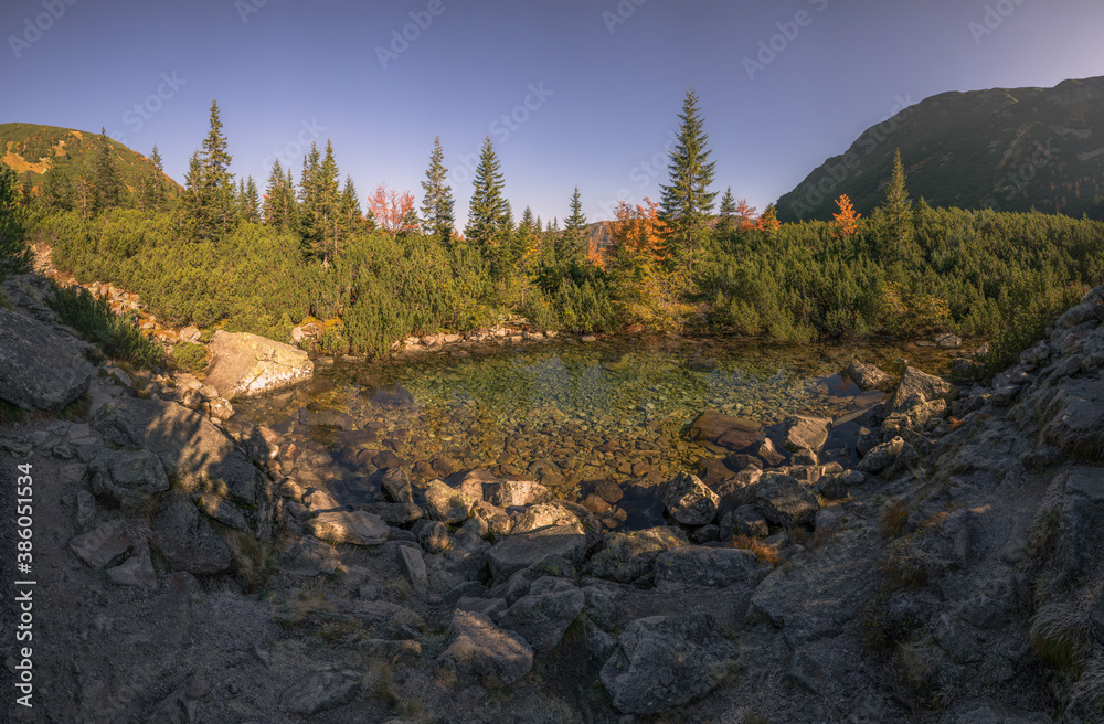 A clear mountain lake surrounded by coniferous trees and stones in the middle of the mountains