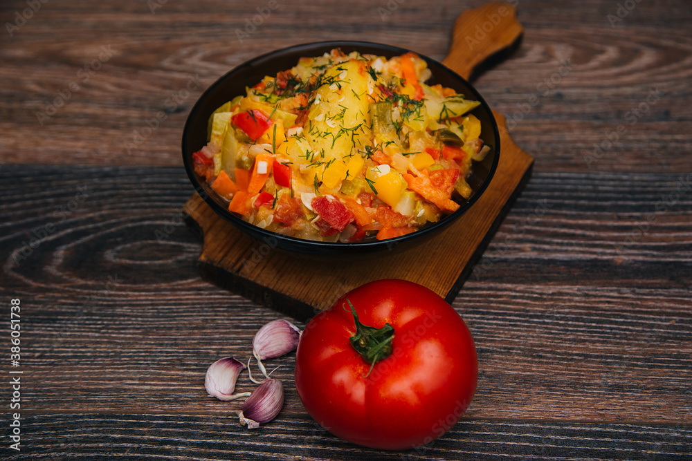 Zucchini ragout in a dark bowl. Vegetable dish for vegetarians on a dark wooden background. Garlic and red tomato Zucchini ragout in a dark bowl. Vegetable dish for vegetarians on a dark wooden background. Garlic and red tomato