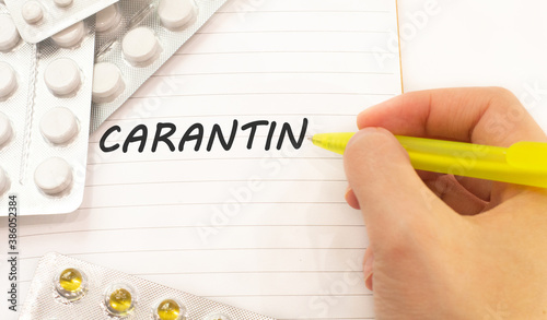 Word carantin written on a white piece of paper. Pills and vitamins lie nearby photo