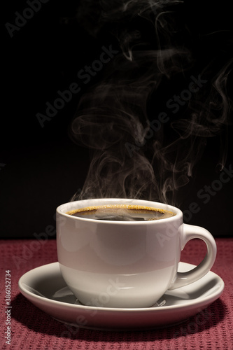 Coffee steaming in a cup with saucer isolated on a black background on a red surface 