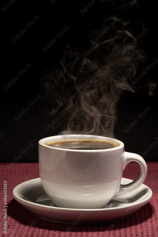 Coffee steaming in a cup with saucer isolated on a black background on a red surface Coffee steaming in a cup with saucer isolated on a black background on a red surface