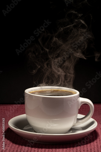 Coffee steaming in a cup with saucer isolated on a black background on a red surface 