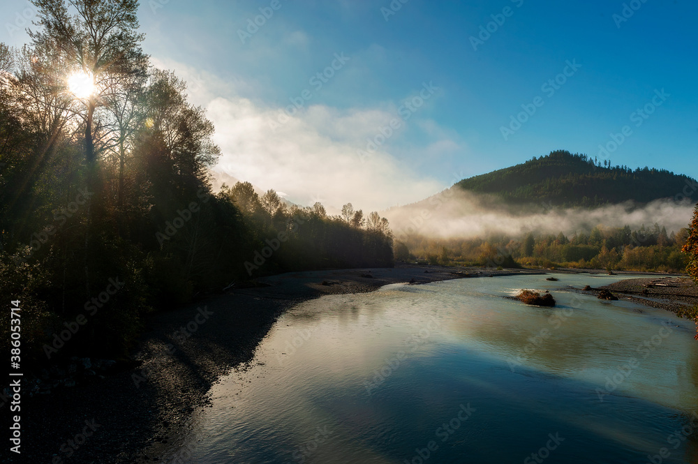 Foggy Morning Along the Nooksack River. Atmospheric view of this beautiful river as fog creeps over the tree line and the sun illuminates the trees and riverbend.