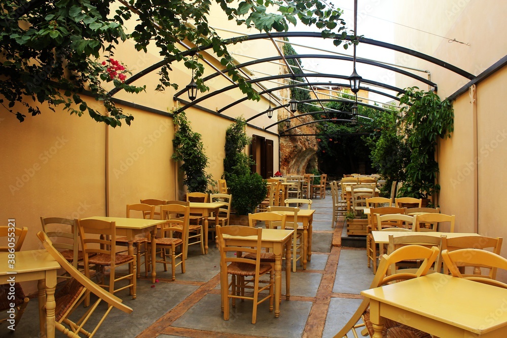 Fototapeta premium Chania, Crete / Greece - August 8th 2015: Empty greek mediterranean restaurant with yellow furniture and lot of green inside in Chania, Crete Island, Greece