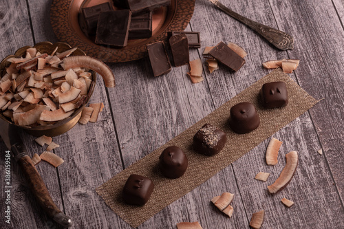 Assorted chocolate handmade praline on dark moody rustic background with dark chocolate chunks and coconut in a shallow background