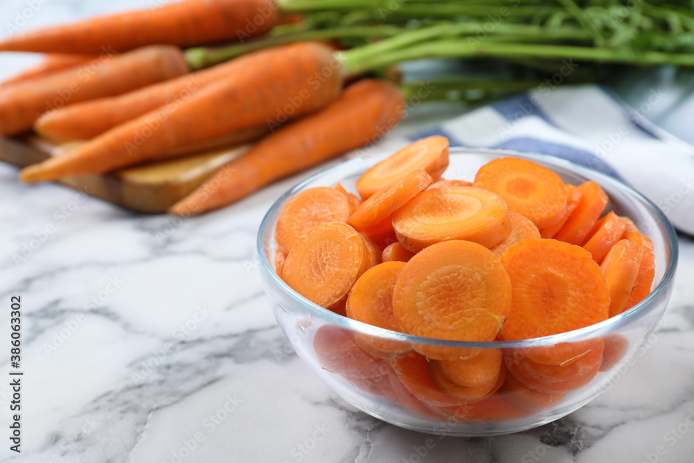 Slices of ripe carrots in glass bowl on white marble table, closeup Slices of ripe carrots in glass bowl on white marble table, closeup