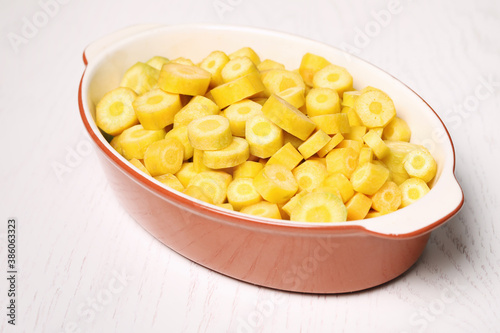 Raw cut yellow carrot in baking dish on white wooden table, closeup