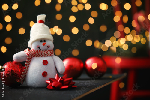 Cute snowman, bow and Christmas balls on table, bokeh effect. Space for text © New Africa