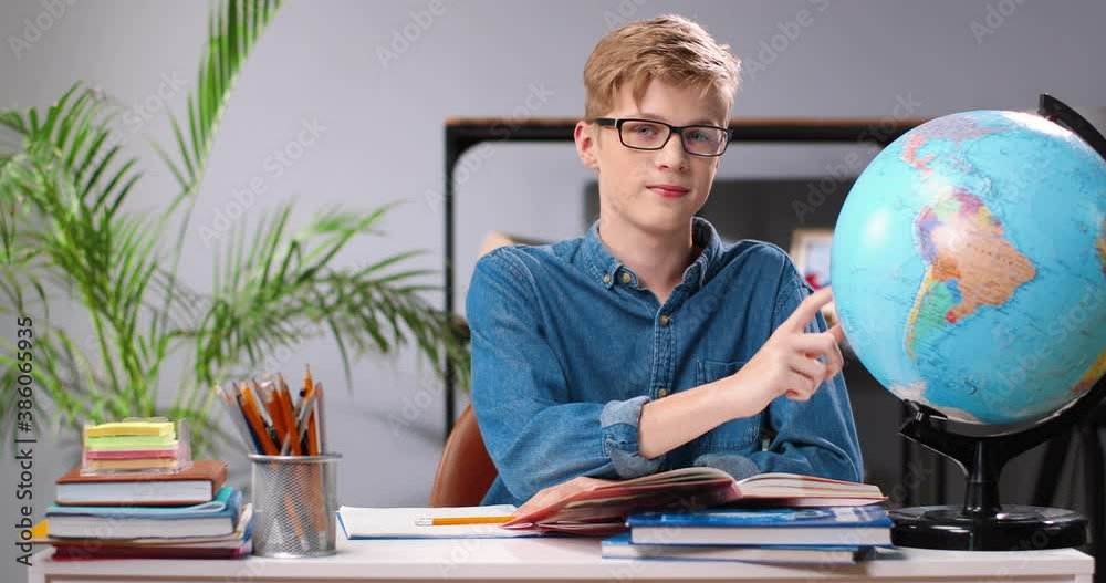 portrait-of-caucasian-teen-boy-in-glasses-learning-geography-with-world