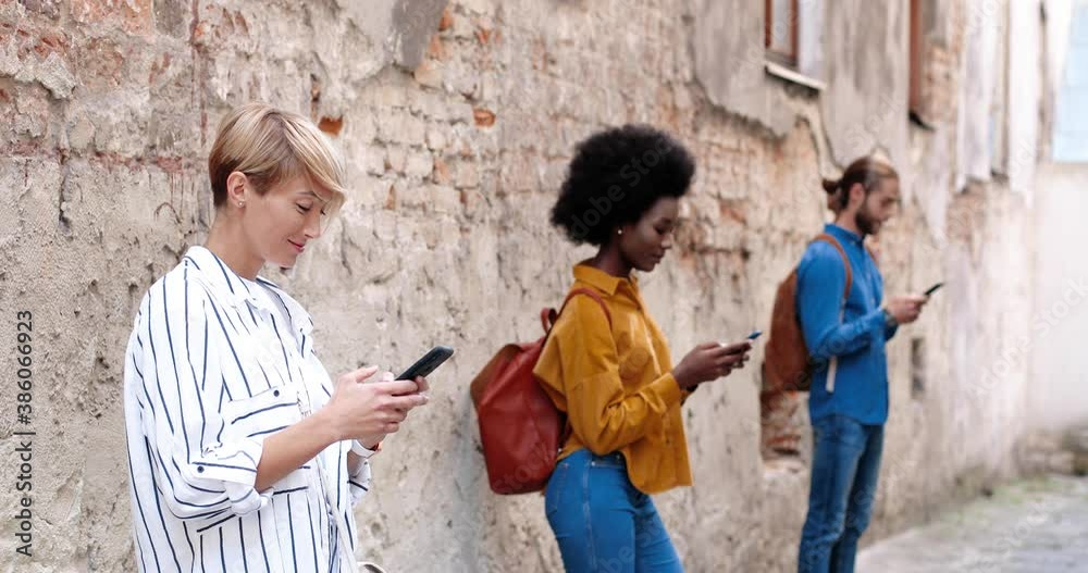 Portrait of beautiful happy Caucasian woman typing on smartphone while standing in old town. African American female browsing cellphone. Woman and man texting on smartphones. Mixed-races concept Portrait of beautiful happy Caucasian woman typing on smartphone while standing in old town. African American female browsing cellphone. Woman and man texting on smartphones. Mixed-races concept
