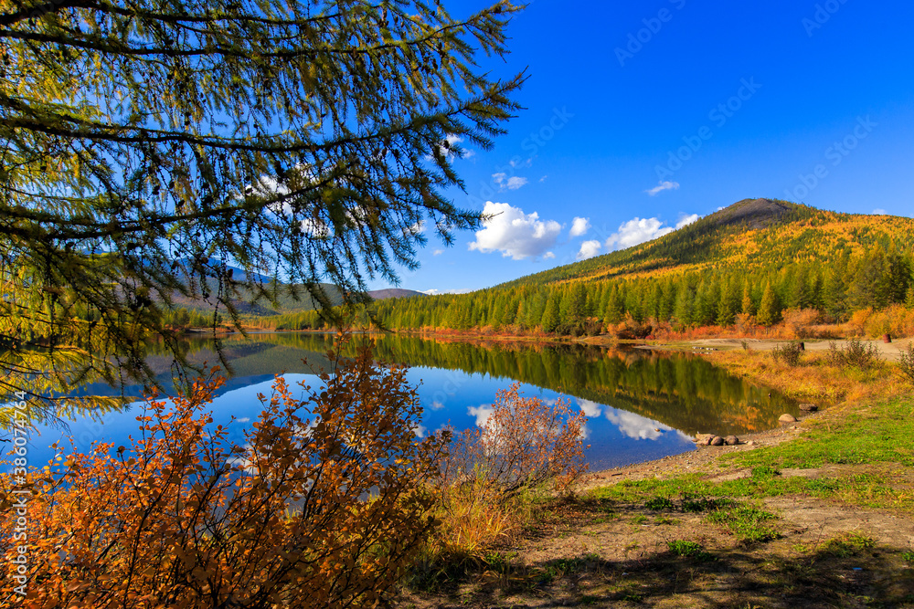 The nature of the Magadan region. A beautiful flat surface of the lake against the background of colored hills and the blue sky. Fascinating view of the forest lake