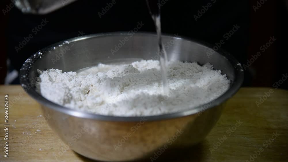 Chef pouring water into a dough bowl while preparing homemade bakery cake over black background Chef pouring water into a dough bowl while preparing homemade bakery cake over black background