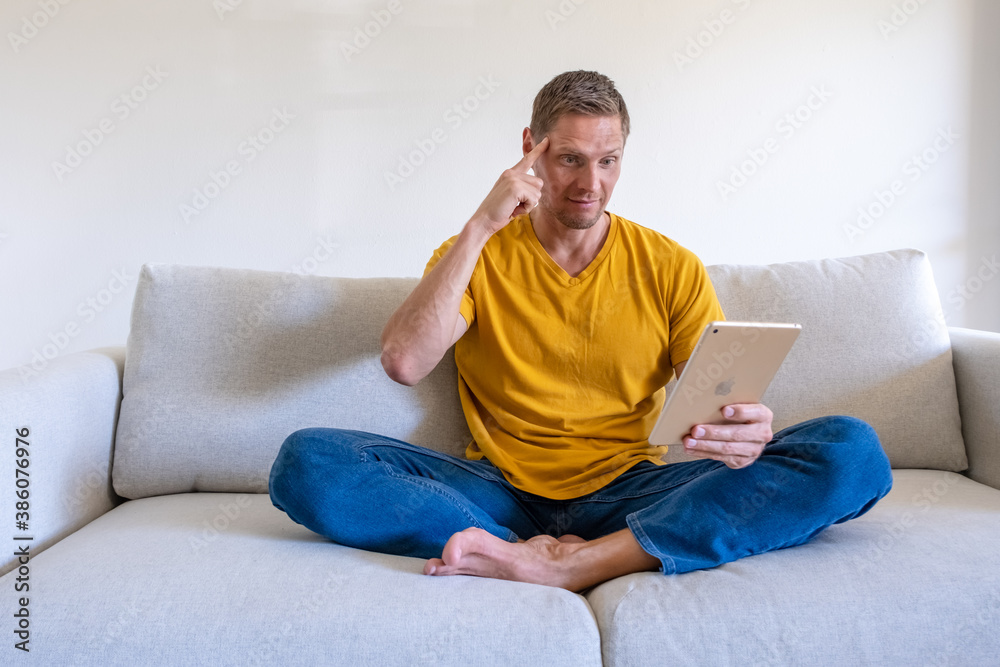 Handsome smiling man using tablet for video calling while relaxing on the couch. Concept for young business people working at home.