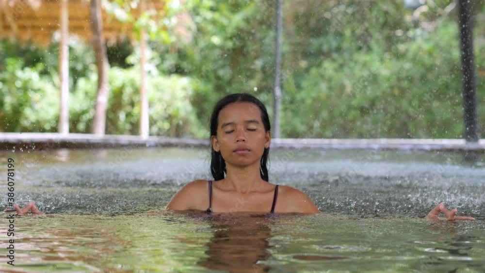 Young woman sitting in water at swimming pool meditating under water fountain. Young woman sitting in water at swimming pool meditating under water fountain.