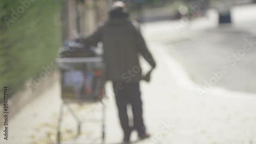 Blurred background of homeless man with a shopping cart walking down a street, in slow motion