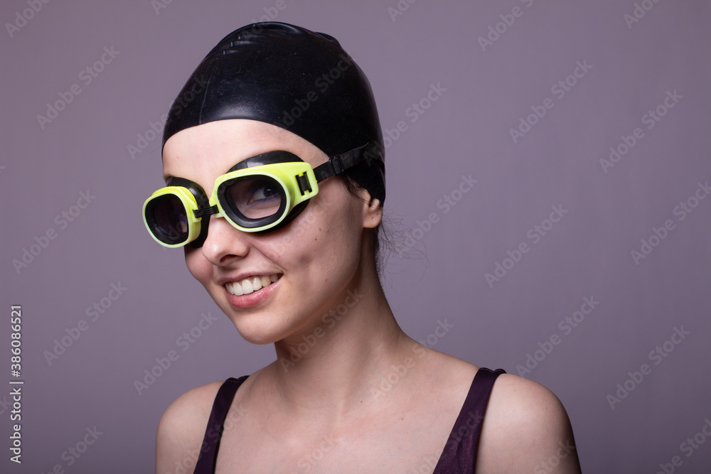 smile woman swimmer, in a swimming cap, glasses and a swimsuit, gray background smile woman swimmer, in a swimming cap, glasses and a swimsuit, gray background