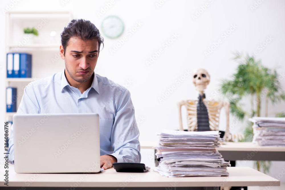 Young male employee and skeleton in the office Young male employee and skeleton in the office
