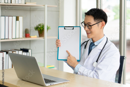 Wallpaper Mural young asian doctor wearing headphone and using computer to give consult to the patient via video call in the hospital office. telemedine and healthcare concept Torontodigital.ca