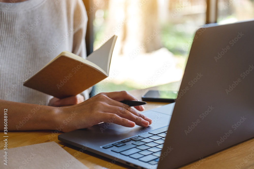 Fototapeta premium Closeup image of a woman writing on a notebook while working on laptop computer in office
