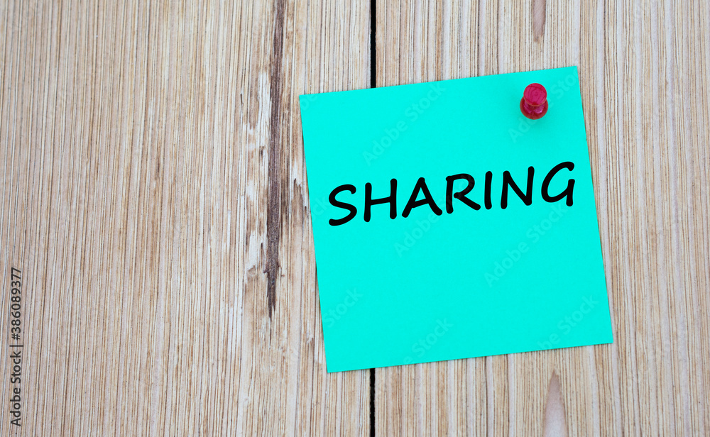 SHARING - word written on a green sheet for notes, which is pinned to a light wooden board SHARING - word written on a green sheet for notes, which is pinned to a light wooden board