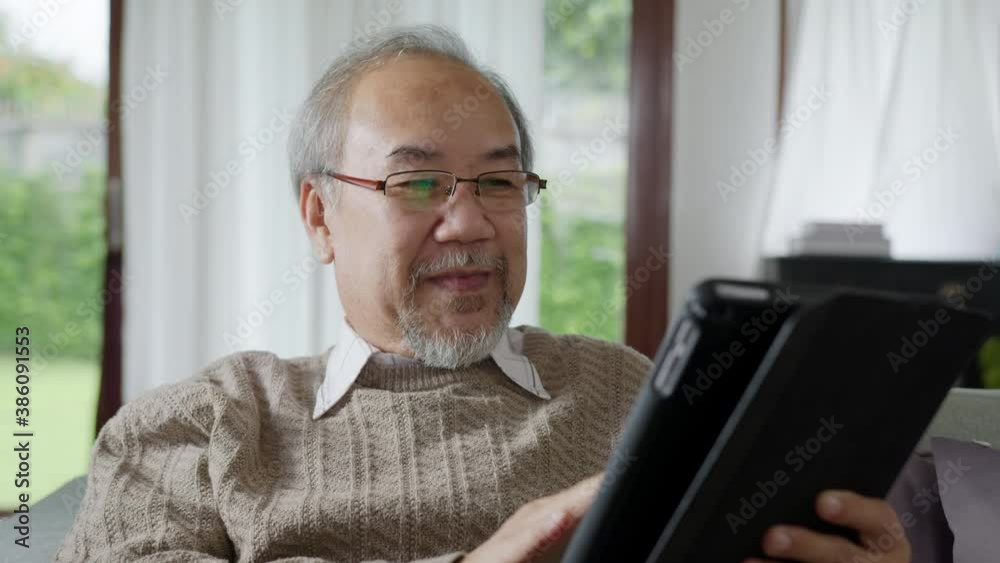 Candid of old asian retired man using tablet computer to transfer money online or financial payment and read text, smile or laugh with happy and positive. Senior asian with digital technology concept Candid of old asian retired man using tablet computer to transfer money online or financial payment and read text, smile or laugh with happy and positive. Senior asian with digital technology concept