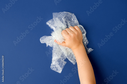 Valokuva Hand popping a bubble wrap on classic blue background, antistress therapy concep