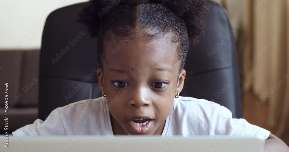 Funny little african girl looking at web camera or screen of laptop