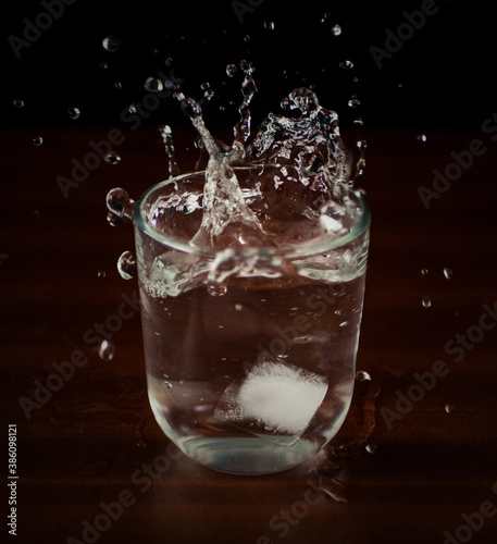 vaso de agua con salpicadura de cubito de hielo en mesa