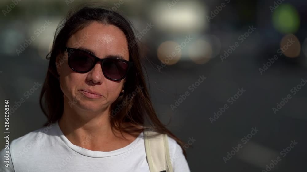 A close-up portrait of a beautiful, dark-haired, smiling middle-aged woman wearing dark glasses. It is located on the background of a highway, cars pass by it. A close-up portrait of a beautiful, dark-haired, smiling middle-aged woman wearing dark glasses. It is located on the background of a highway, cars pass by it.