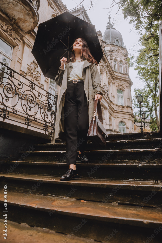 young pretty woman in autumn outfit walking by city street with umbrella at rainy weather young pretty woman in autumn outfit walking by city street with umbrella at rainy weather