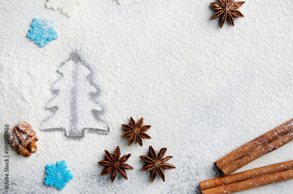 Christmas kitchen background made of flour, cinnamon sticks, anise, cookie cutter and sugar sprinkles