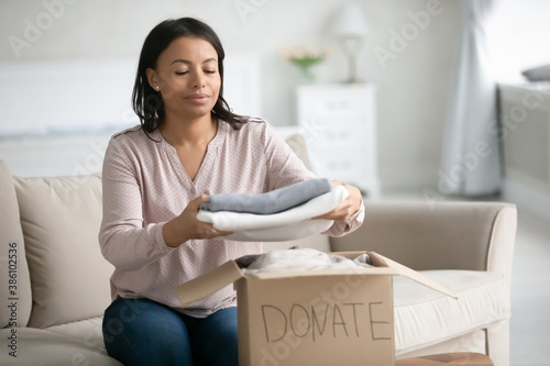 Фотография Caring African American woman sit at home put stuck clothes in donation box at home
