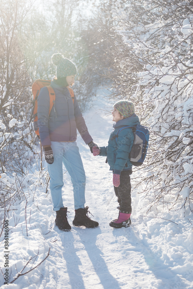 A child with a backpack walks with mother in a snowy forest