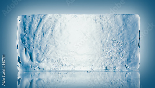 The rectangular block of pure transparent ice in cold blue tones on a mirroring surface with reflection.