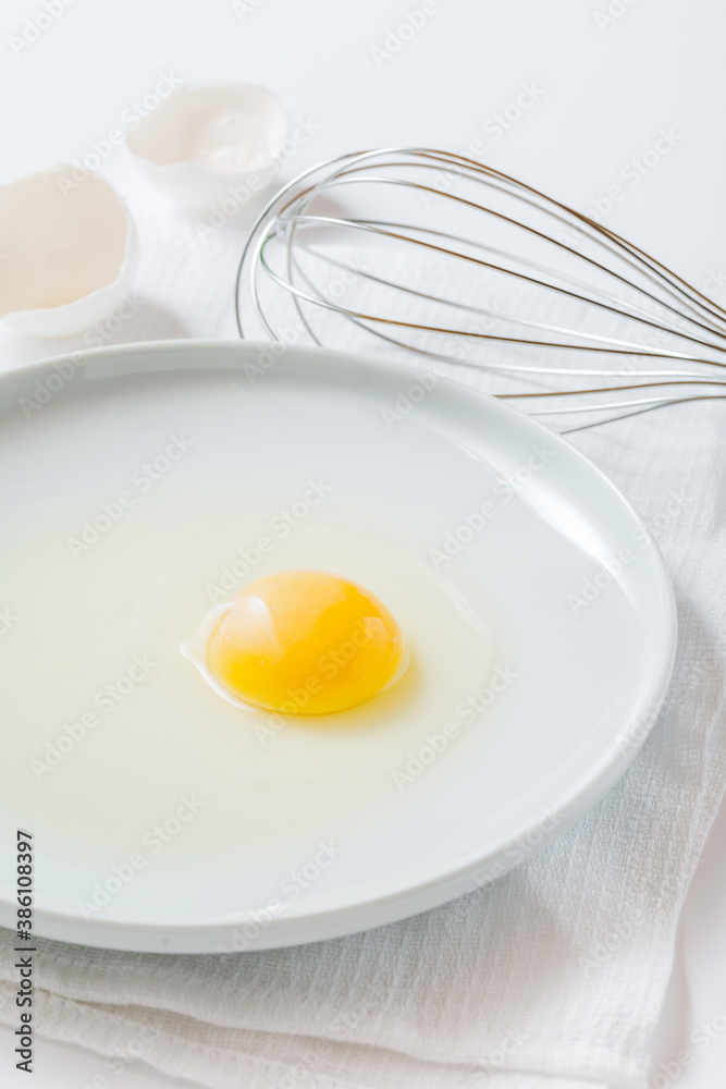 egg yolk on a plate  and whisk on white