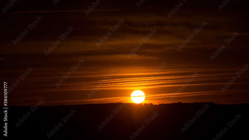 Disc of the sun over the horizon in the sunset sky with striped clouds