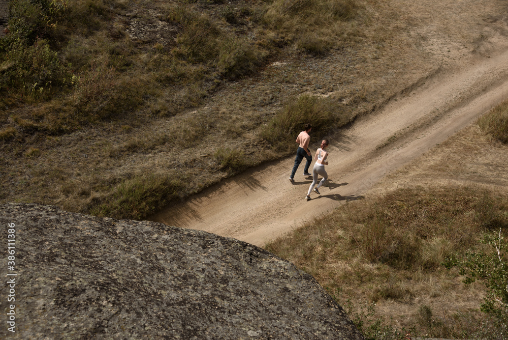A guy and a girl in sportswear run along a mountain road, view from above.
