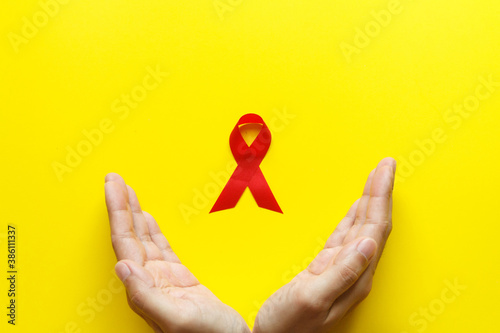 red AIDS awareness ribbon on yellow paper background. World aids day and healthcare and medicine concept