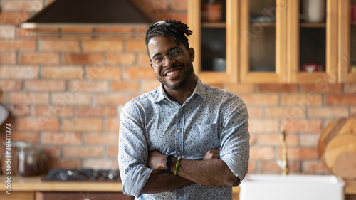 Portrait of smiling millennial African American man in glasses pose in modern renovated home kitchen. Happy young 20s biracial male tenant or renter in spectacles satisfied with good quality service. photo