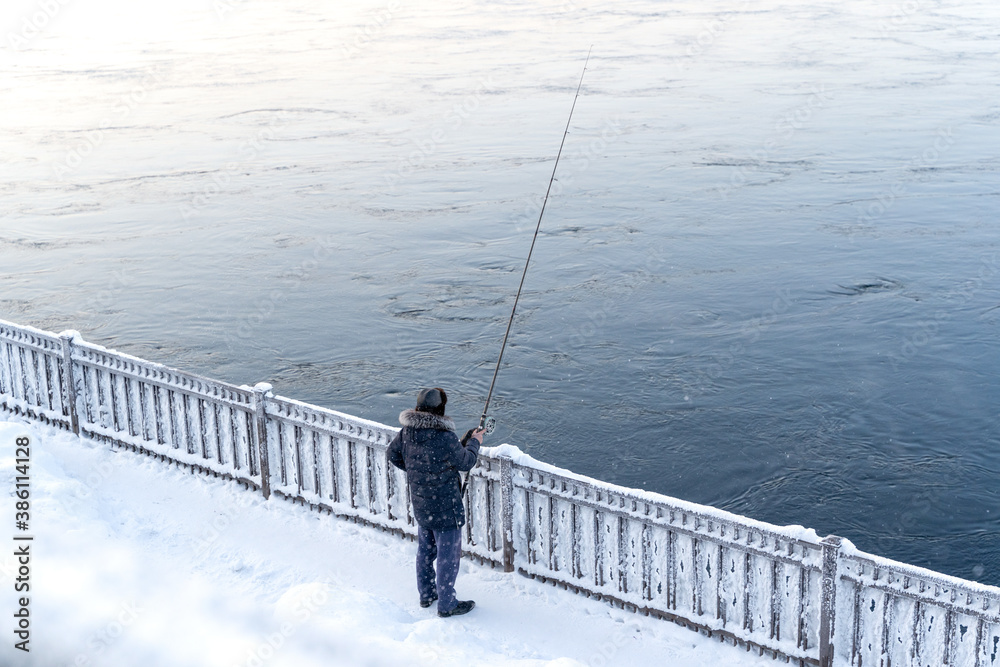 One fisherman is fishing on city river side in extreamly cold weather in winter