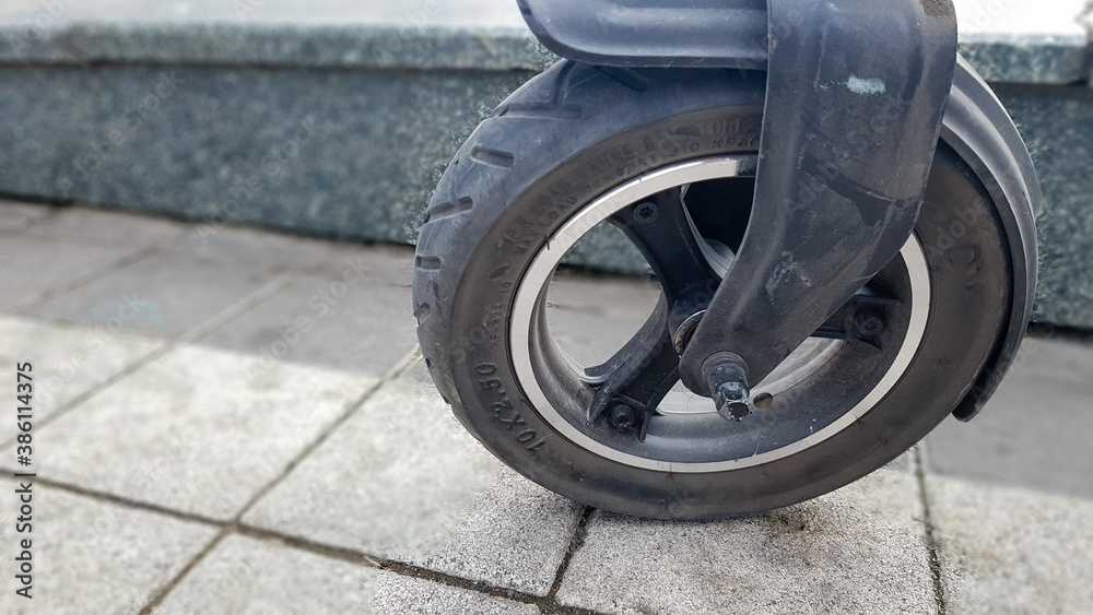 Scratched and damaged front wheel of an electric scooter on a city street against the background of paving slabs. Old e-scooter wheel. Modern technologies. Eco transport is provided for rent.