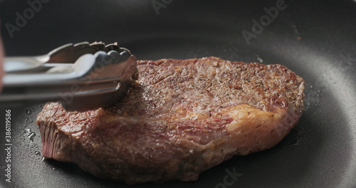 Closeup shot of man hands flip ribeye steak on non stick pan with steel tongs