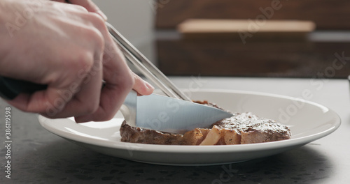 Man slicing ribeye steak on a white plate on concrete countertop