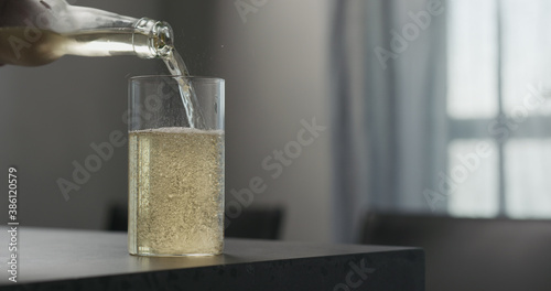 Photos man pour soda drink from a bottle into highball glass on concrete countertop wit